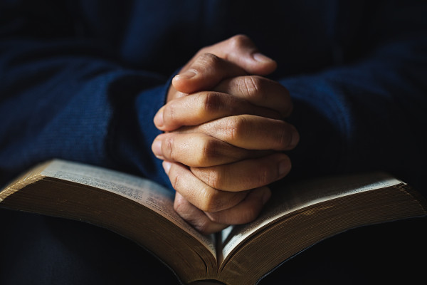 Hands folded in prayer over a bible